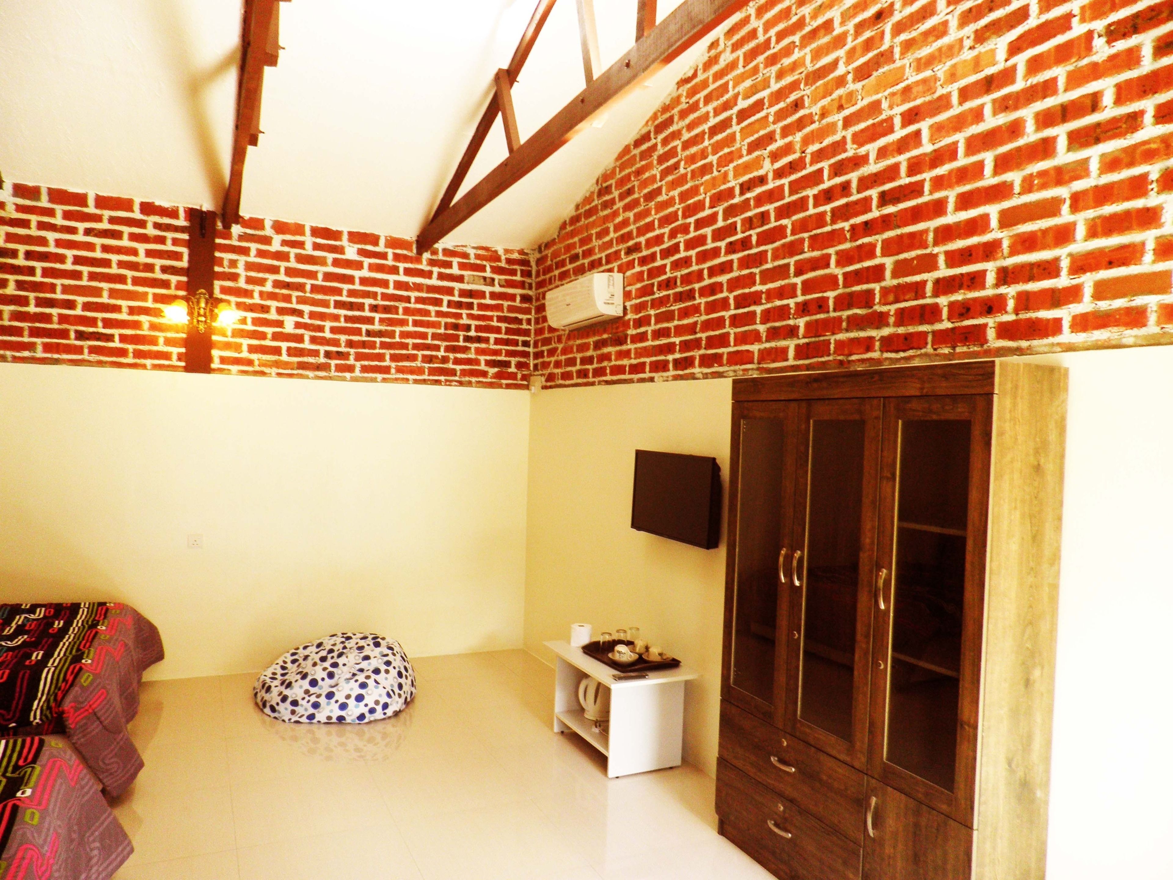 Una habitación con pared de ladrillo, un armario de madera, un estante blanco y un sillón de peluche a lunares.