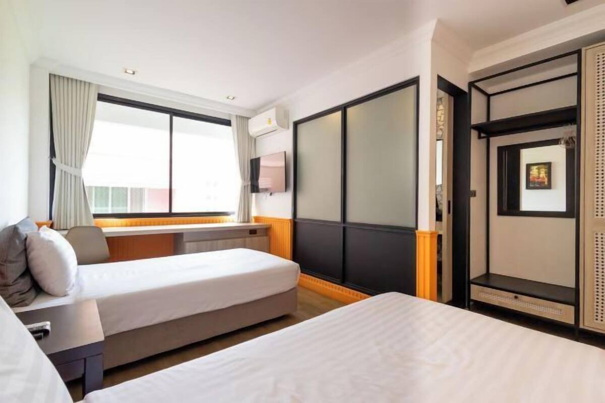 A hotel room with two beds, a window with curtains, a television, and a wardrobe.