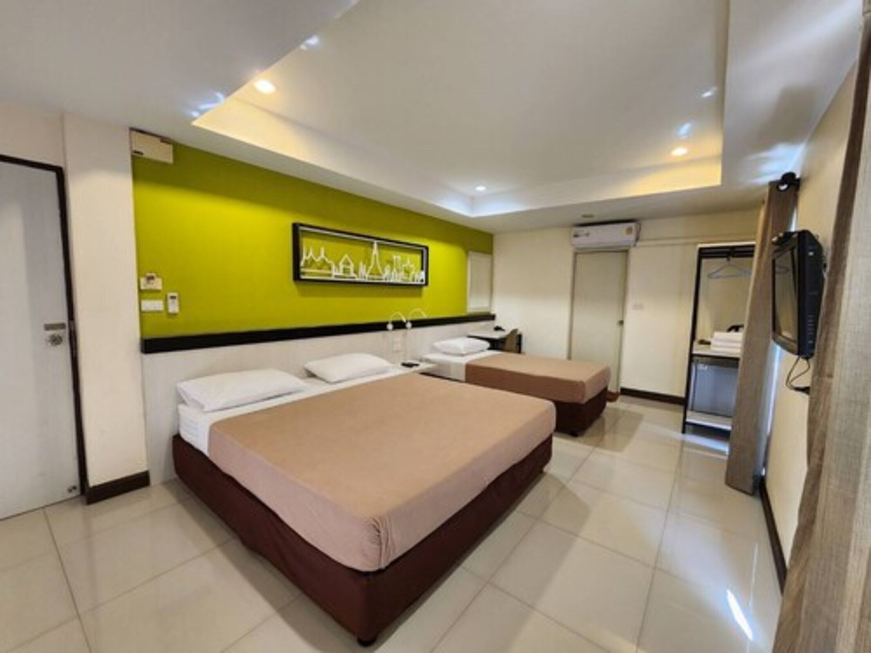 A hotel room with two beds, a green accent wall, a framed artwork, and a television.
