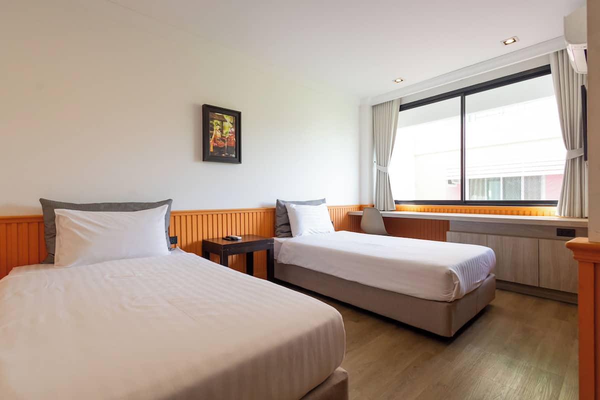 A hotel room with two beds, a desk, a chair, a window with curtains, and a wall-mounted picture.
