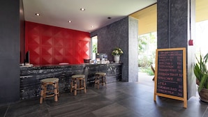 A modern reception area with a black marble counter, red geometric wall, and three wooden stools. A chalkboard menu lists breakfast items and prices. - Penpark Place (Bangkok)