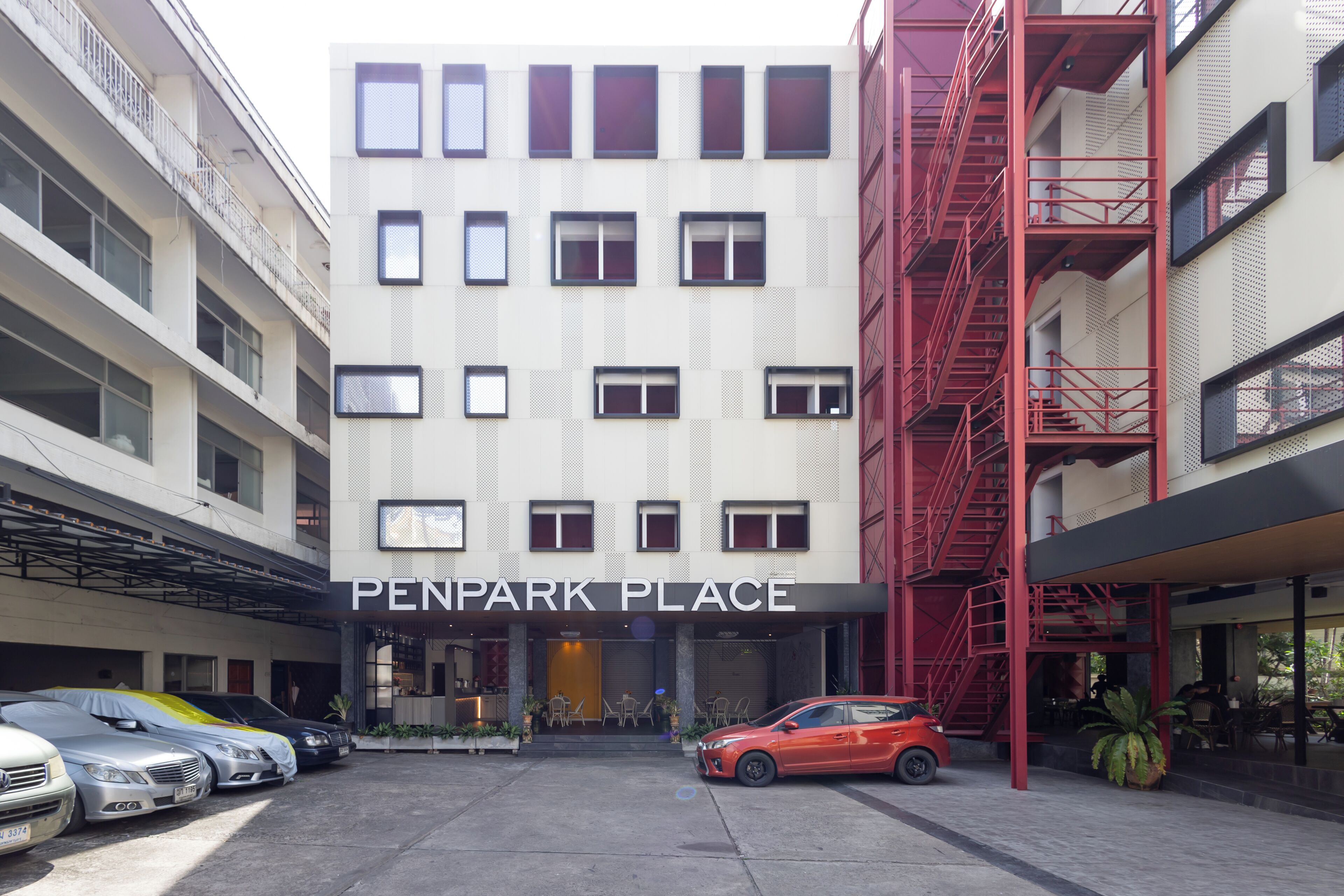 A multi-story building with a sign reading "PENPARK PLACE" at the entrance. There are several parked cars in front, including a red car.