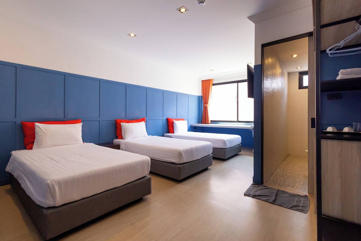 A hotel room with three beds, a wooden floor, and a view of the outside.