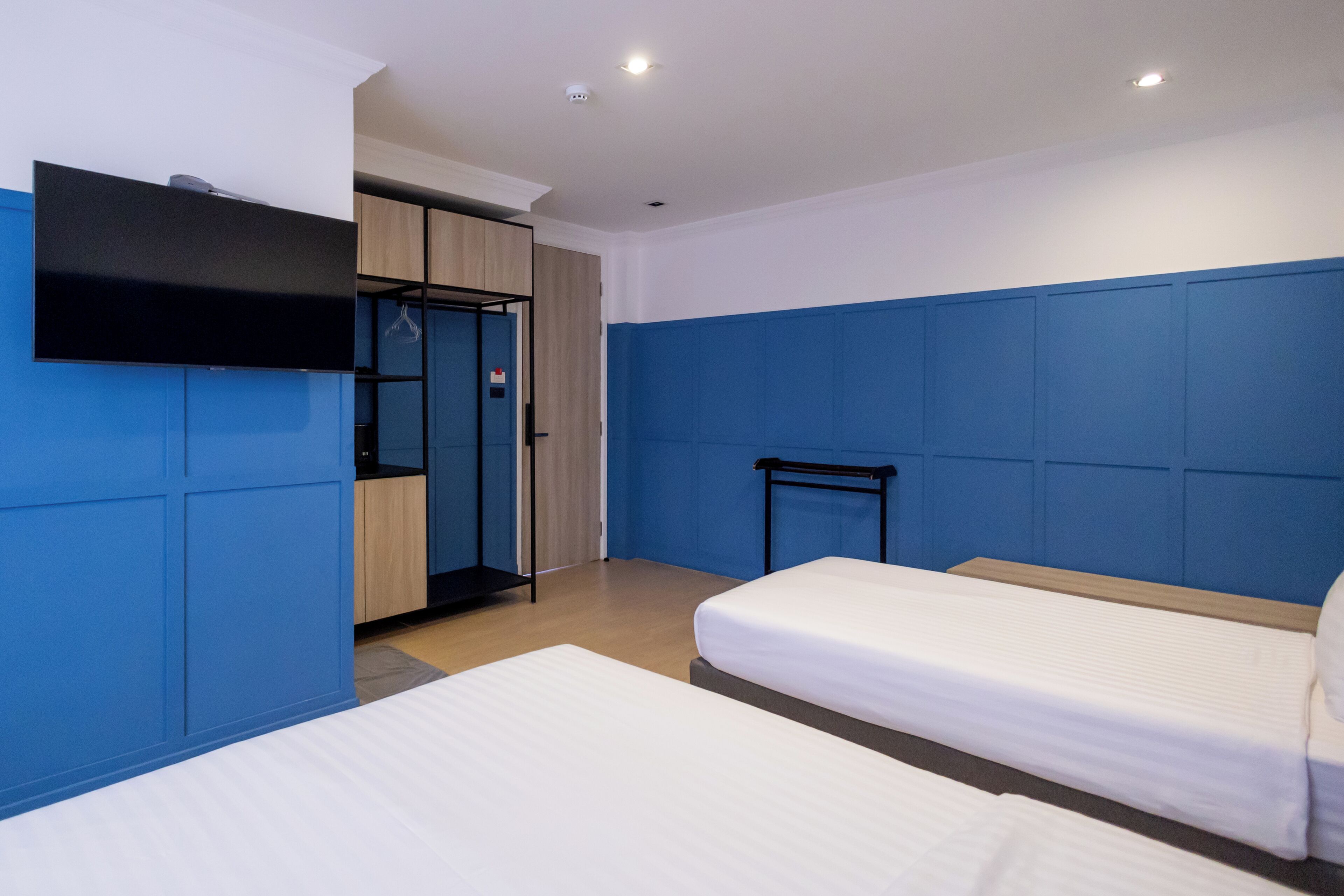 Een hotelkamer met twee bedden, een aan de muur bevestigde televisie en een kledingkast.