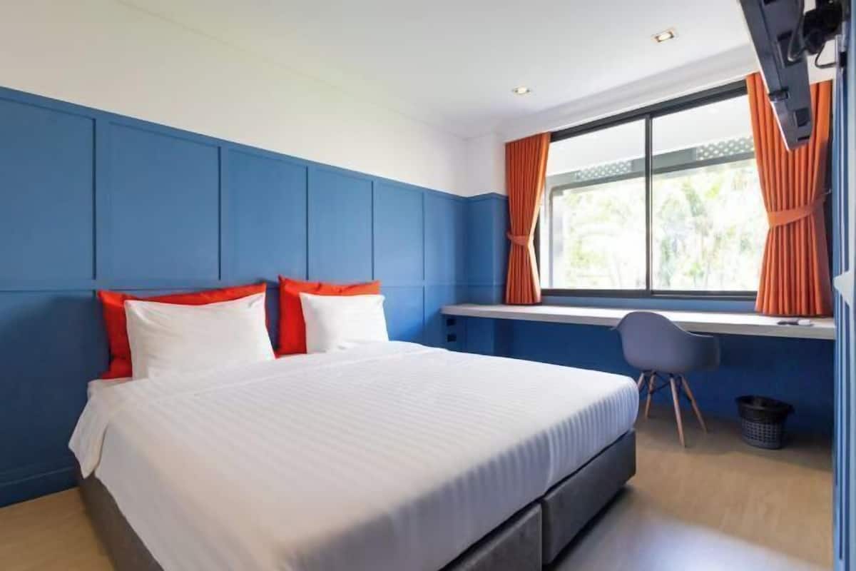 A bedroom with a bed, a desk, and a window with curtains.