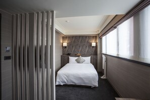 A hotel room with a bed, two wall-mounted lamps, a patterned headboard, and a window with curtains. - Citizen Hotel (Taipei)