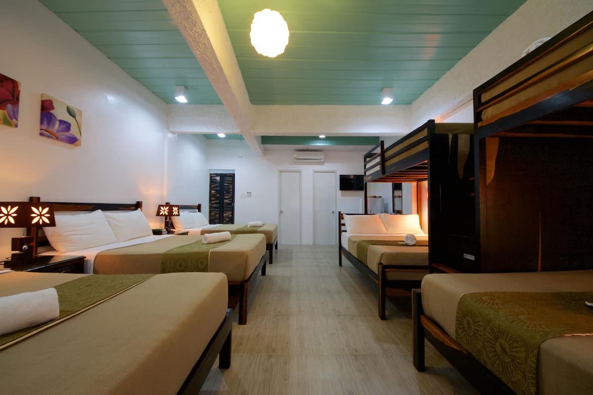 A hotel room with four beds arranged in a row, a television, and a door leading to another room.