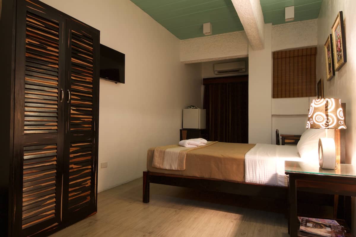 A bedroom with a bed, a wardrobe, a bedside table with a lamp, and a window with blinds.