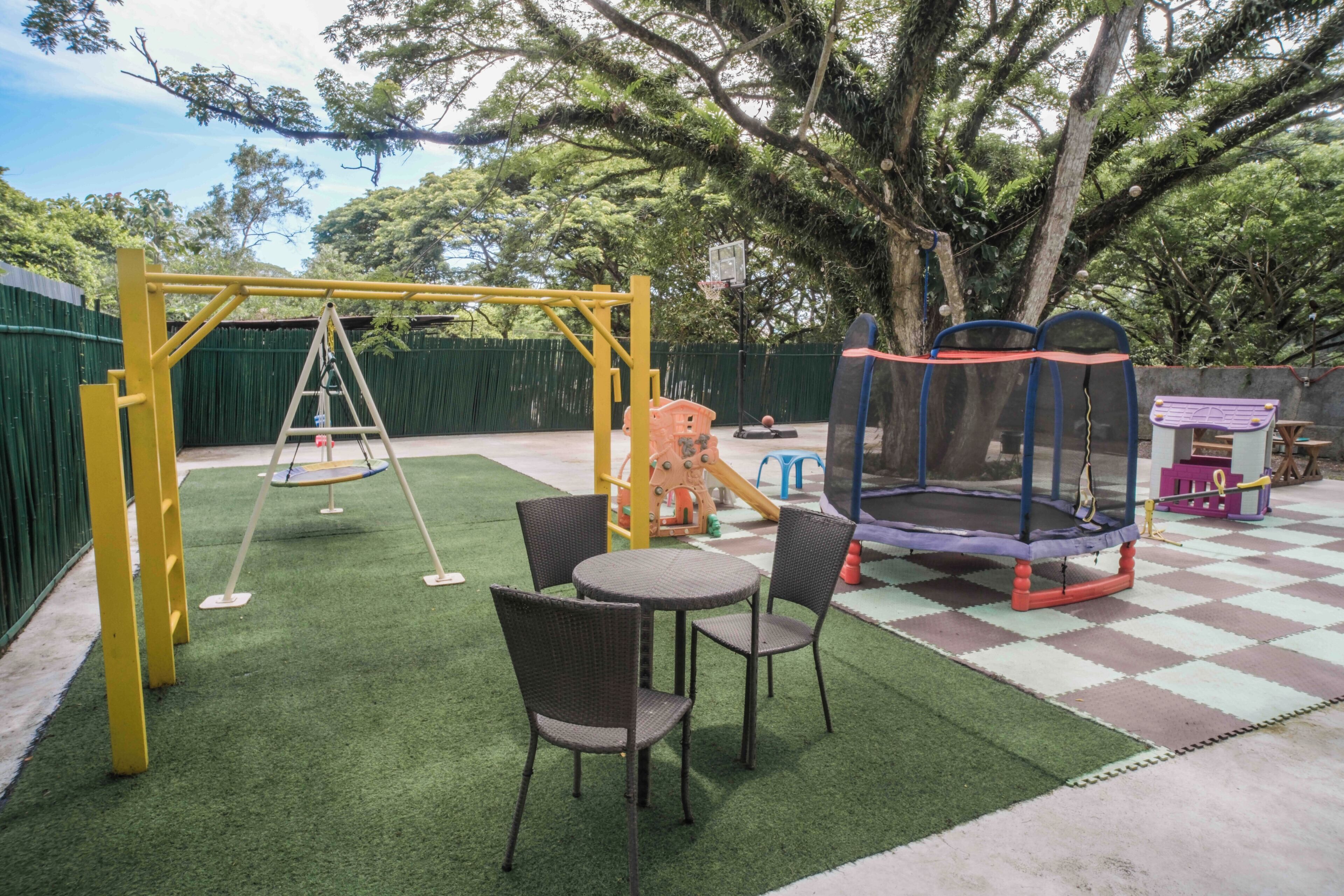 A playground with a swing set, a trampoline, and a table with chairs.
