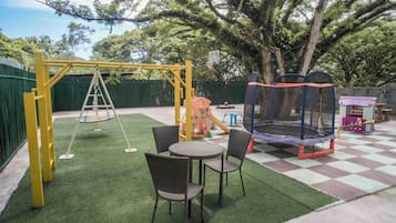 A playground with a swing set, a trampoline, and a table with chairs.