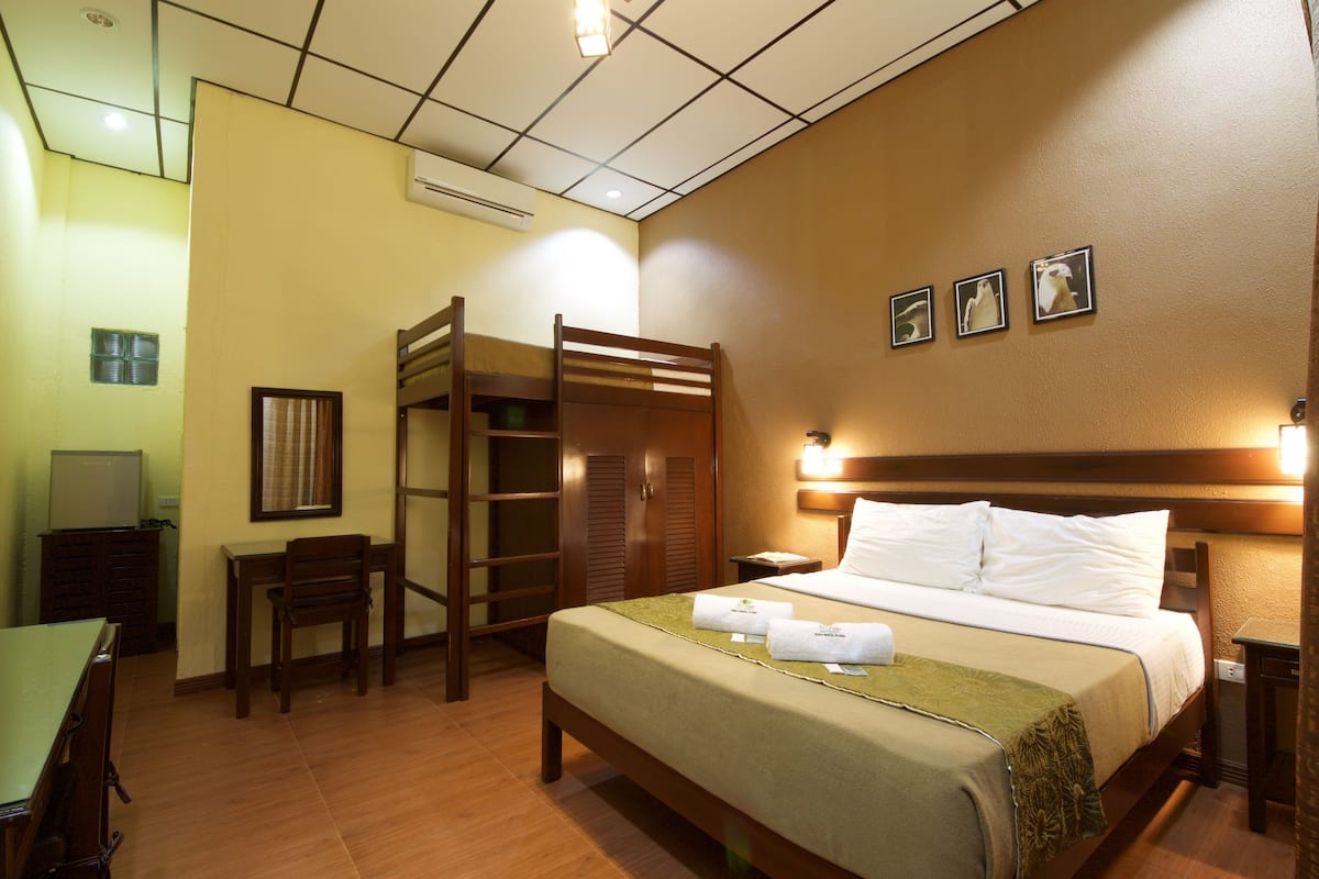 A hotel room with a bunk bed, a desk, a chair, a bedside table, and a wall-mounted TV.