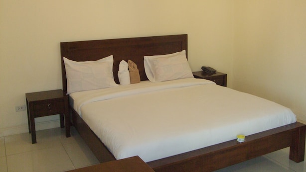 A neatly made bed with white linens, a wooden headboard, and a bedside table with a phone and a small container. - Baan Kittima (Pattaya)