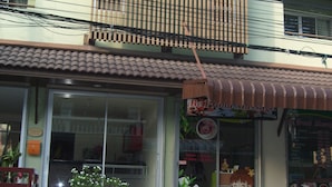 A building with a storefront featuring a sign for a massage service. There is a potted plant and a white plastic chair outside. - Baan Kittima (Pattaya)