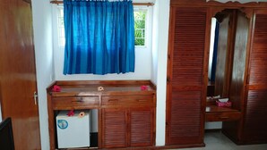 A room with a wooden desk, a small refrigerator, a window with blue curtains, and a wooden wardrobe. - C'est Mon Choix (Praslin Island)