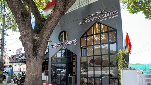 A building with a large tree in front, a sign for 'Aishwarya Suites,' and another sign for 'Grillies.' - Aishwarya Suites (Mysore)