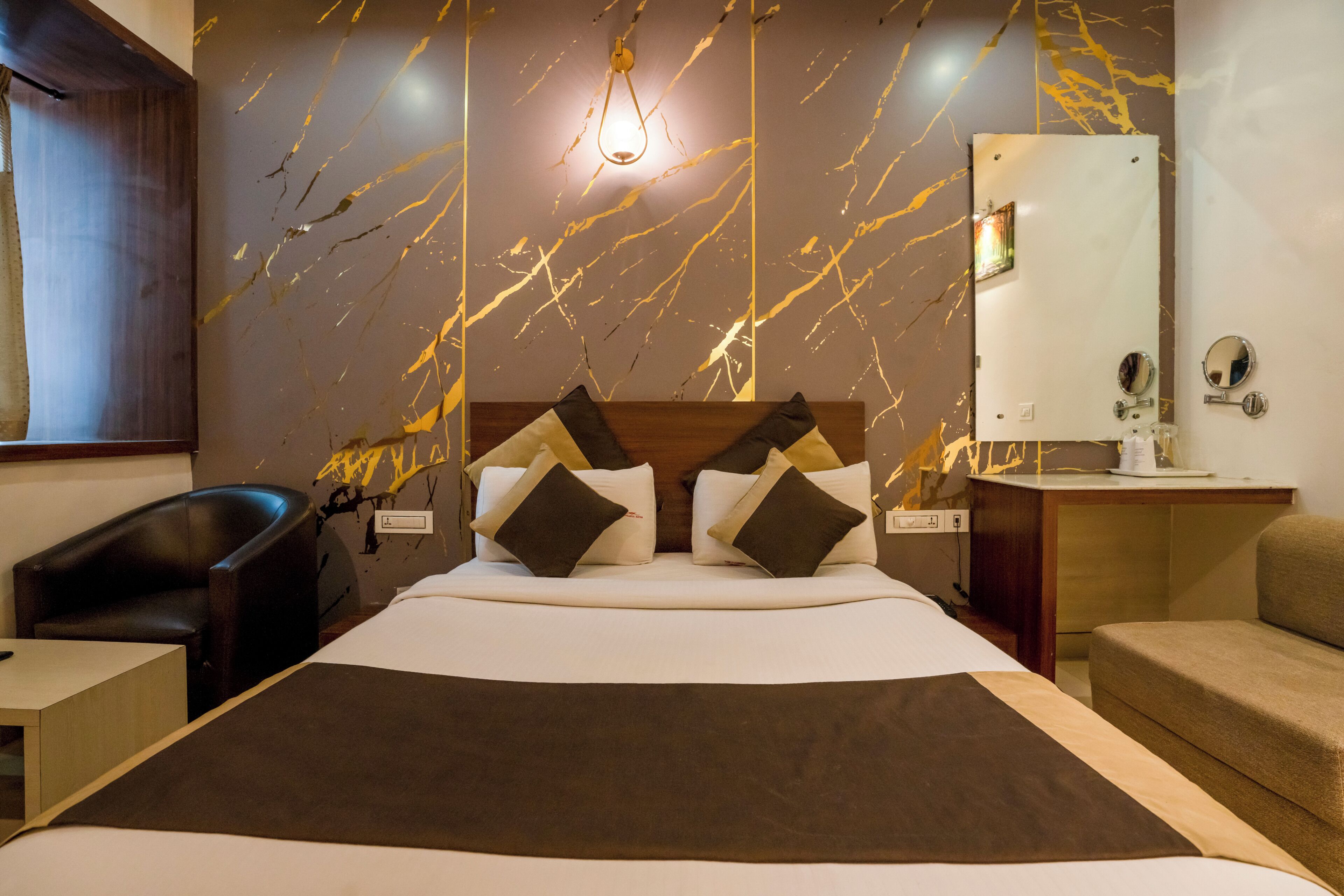 Habitación de hotel con cama, escritorio, silla, espejo y pared con diseño tipo mármol.
