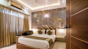A modern hotel room with a bed, bedside tables, a desk, and an air conditioning unit. - Aishwarya Suites (Mysore)