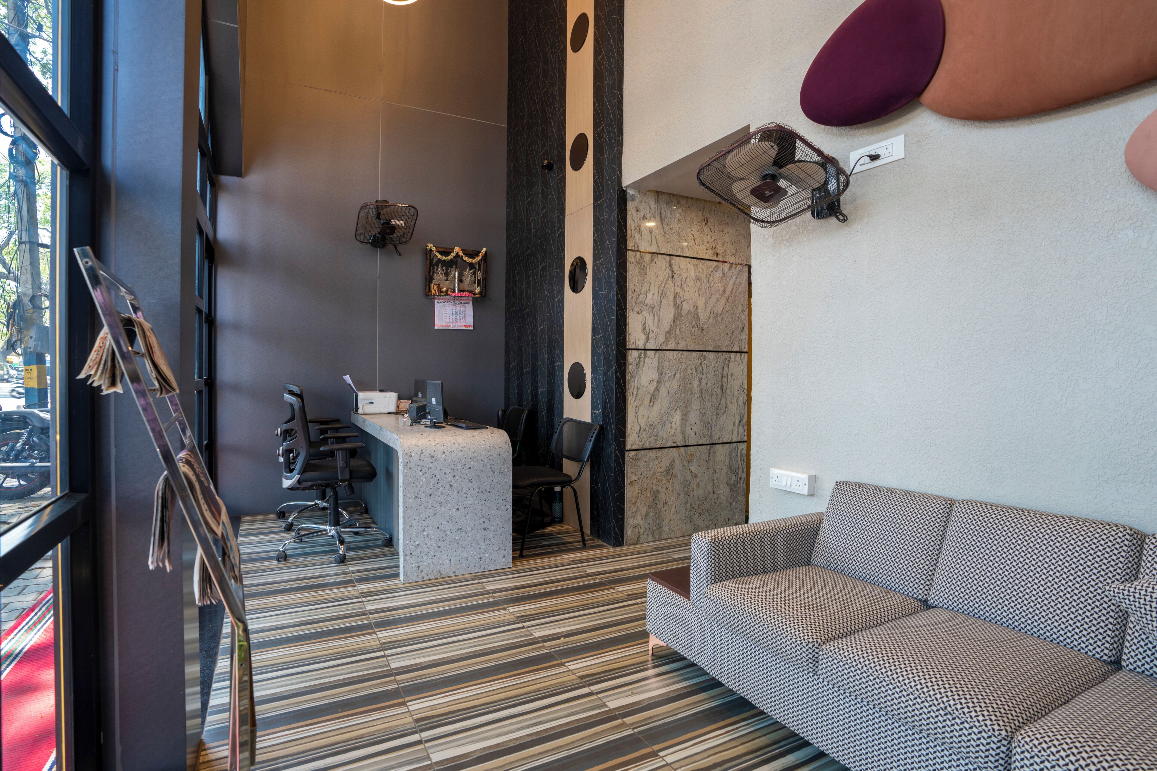 A reception area with a reception desk, office chairs, a patterned sofa, and a wall-mounted fan.