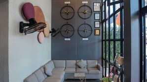 A modern interior with a sectional sofa, wall-mounted clocks, and a large window. - Aishwarya Suites (Mysore)