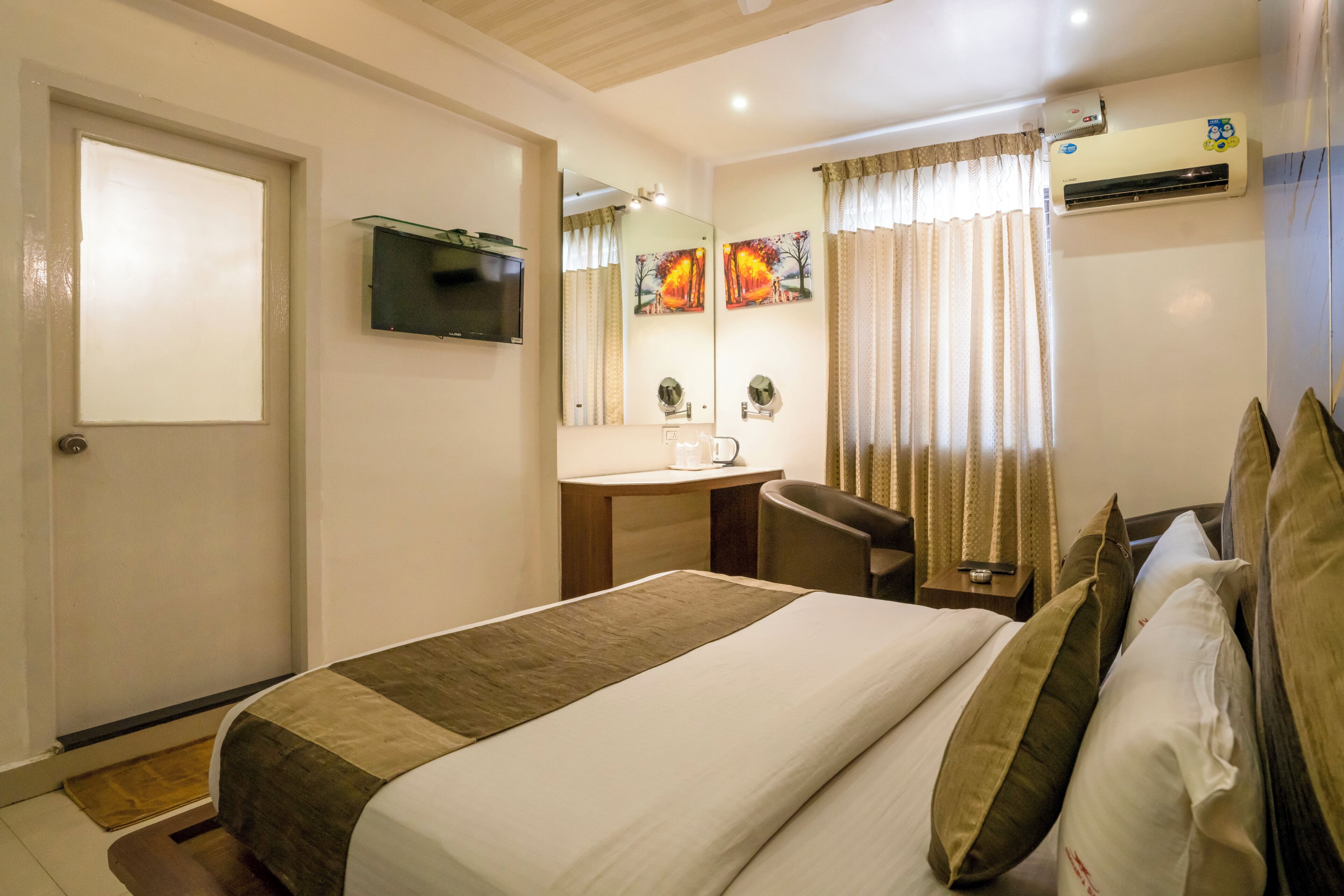 Une chambre d’hôtel équipée d’un lit, d’un bureau, d’une chaise, d’une télévision, d’un miroir, d’un climatiseur et d’une fenêtre avec des rideaux.