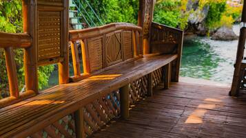 Una terraza de madera con banco, barandillas y una estructura de techo de paja.