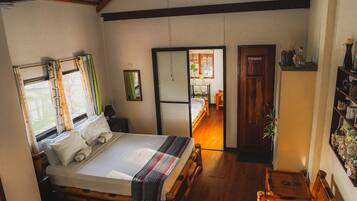 A room with a bed, wooden floor, ceiling fan, and a door leading to another room.