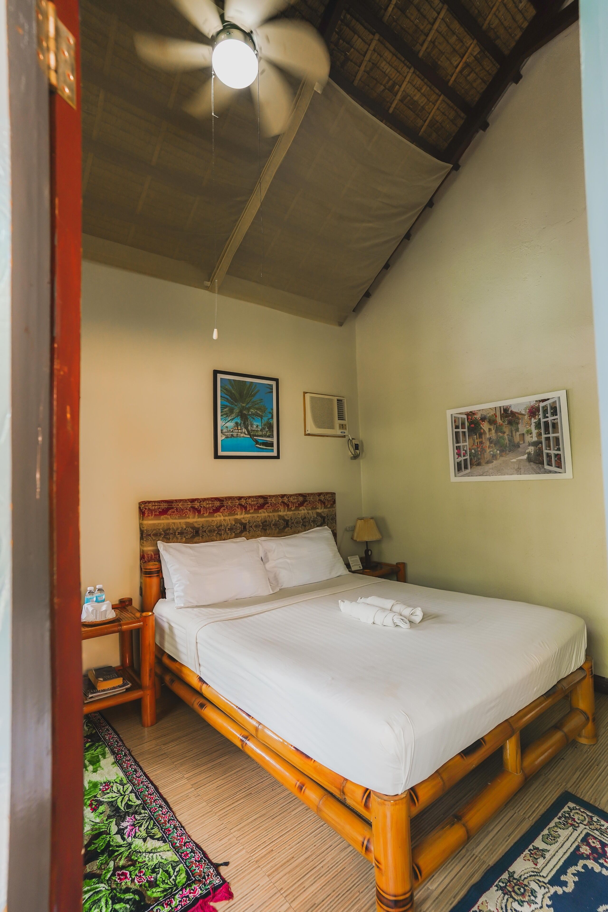 A room with a bed, a ceiling fan, a nightstand, a lamp, and a wall-mounted air conditioner.
