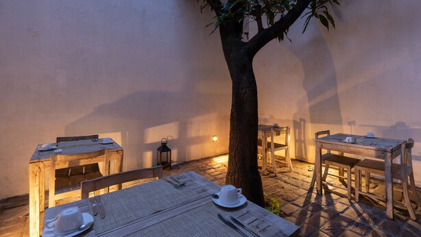 A rustic outdoor dining area with wooden tables and chairs, a tree, and a lantern. - Rockwell Colombo (Colombo)