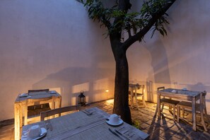 A rustic outdoor dining area with wooden tables and chairs, a tree, and a lantern. - Rockwell Colombo (Colombo)