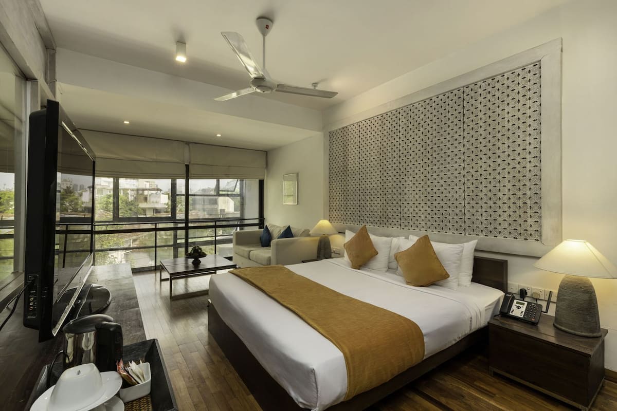A modern hotel room with a large bed, a sofa, a desk, and a view of the city.