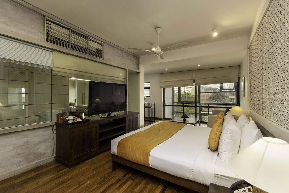 A modern hotel room with a large bed, a TV, a desk, and a balcony with a view.