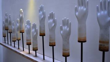 A row of white, hand-shaped sculptures with varying sizes and a few with brownish discolorations, mounted on black stands on a wooden shelf against a plain wall.