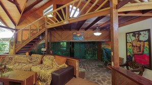 A wooden interior with a staircase, a sofa, a painting, and a stone floor. - Chosa Manglar Nature Retreat (Puerto Jiménez)