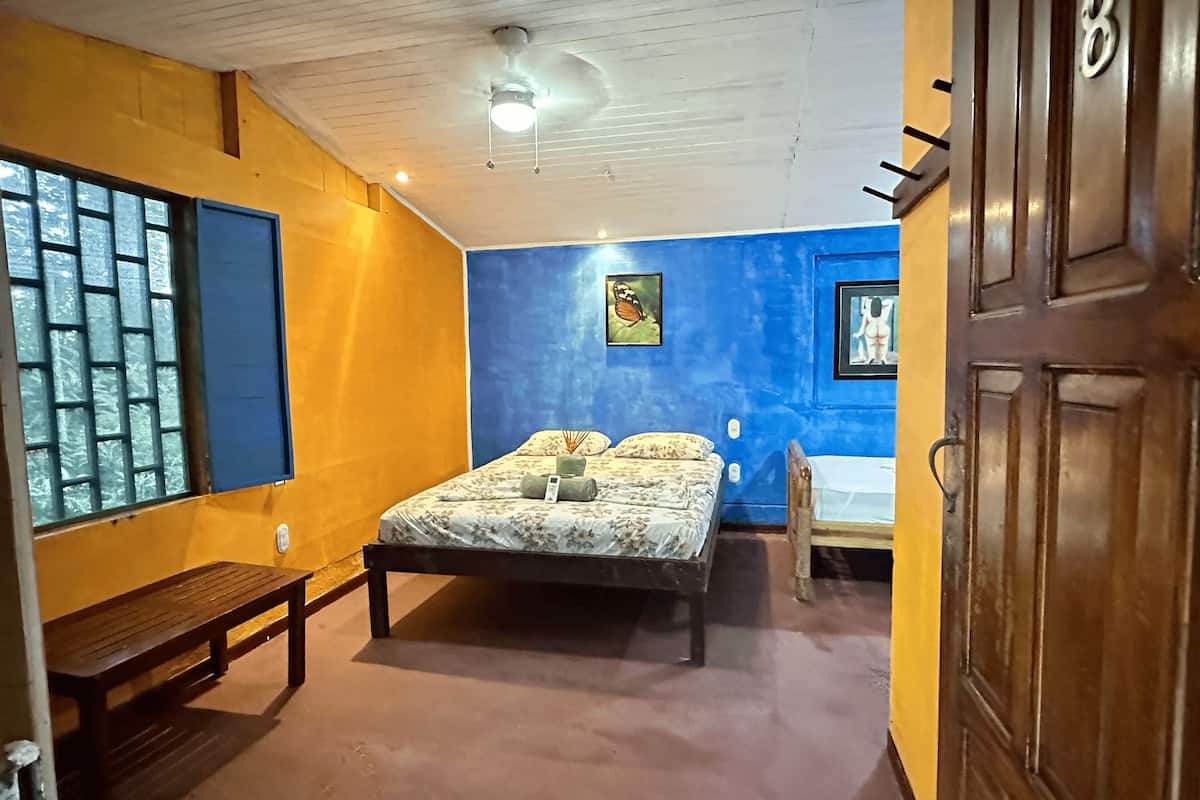 Een slaapkamer met een bed, een bankje, een plafondventilator en een deur met een nummer.