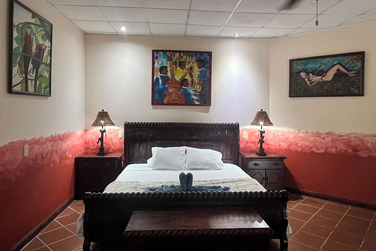 Een hotelkamer met een bed, twee bedlampen, een plafondventilator en drie schilderijen aan de muur.