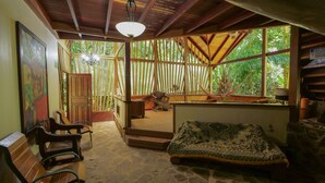 A rustic wooden room with a large window, a hammock, and a patterned sofa. - Chosa Manglar Nature Retreat (Puerto Jiménez)