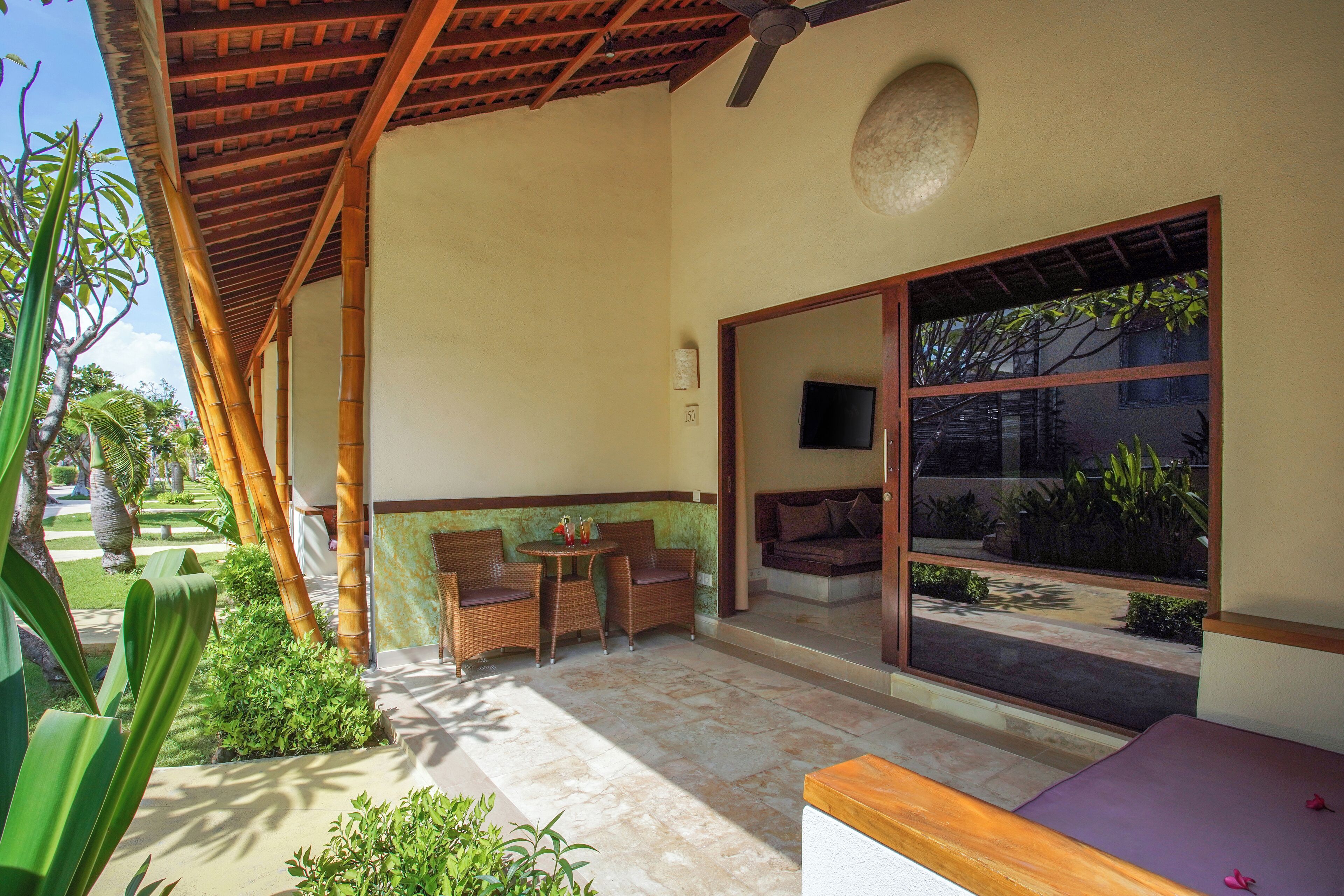 A covered outdoor seating area with a table and chairs, a sofa, and a large window overlooking a garden.