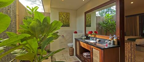 Une salle de bain moderne avec un grand miroir, un lavabo et des toilettes. On y trouve également des plantes et une fenêtre qui laisse entrer la lumière naturelle.