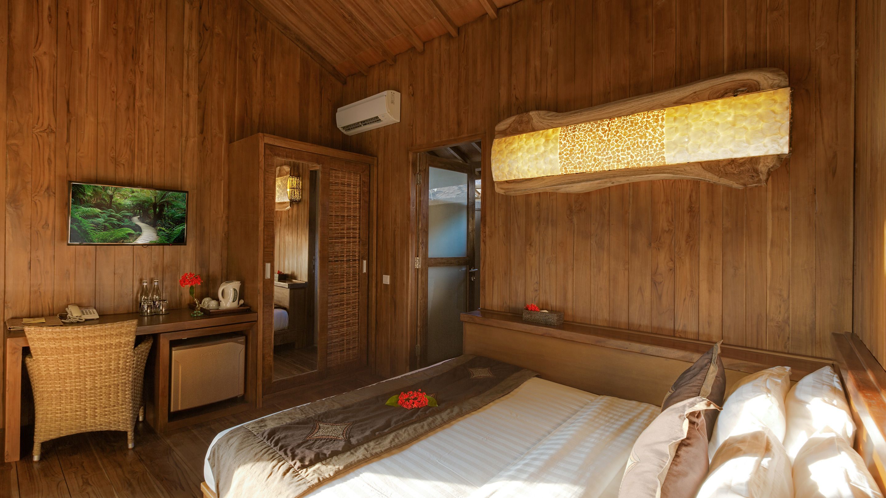A wooden room with a bed, a desk, a television, and a bathroom visible through an open door.