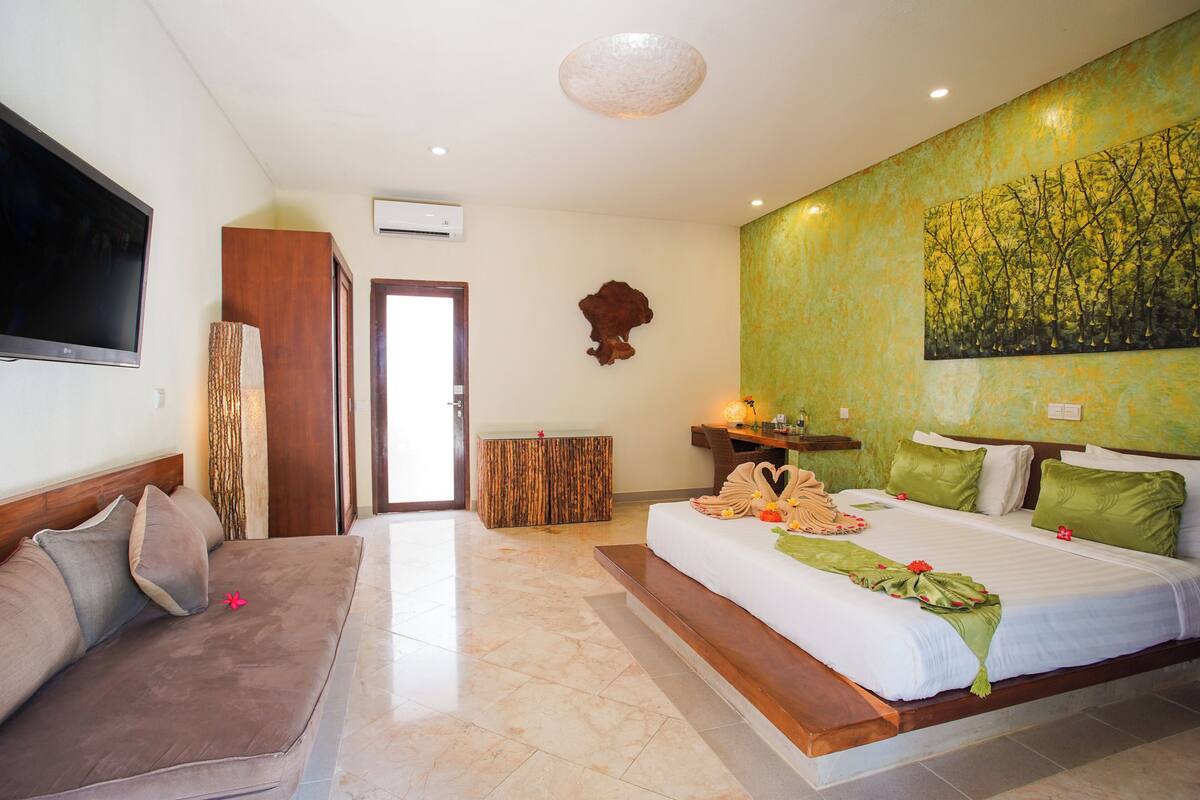 Habitació d'hotel amb llit, un sofà, televisió, armari de fusta i un quadre penjat a la paret.