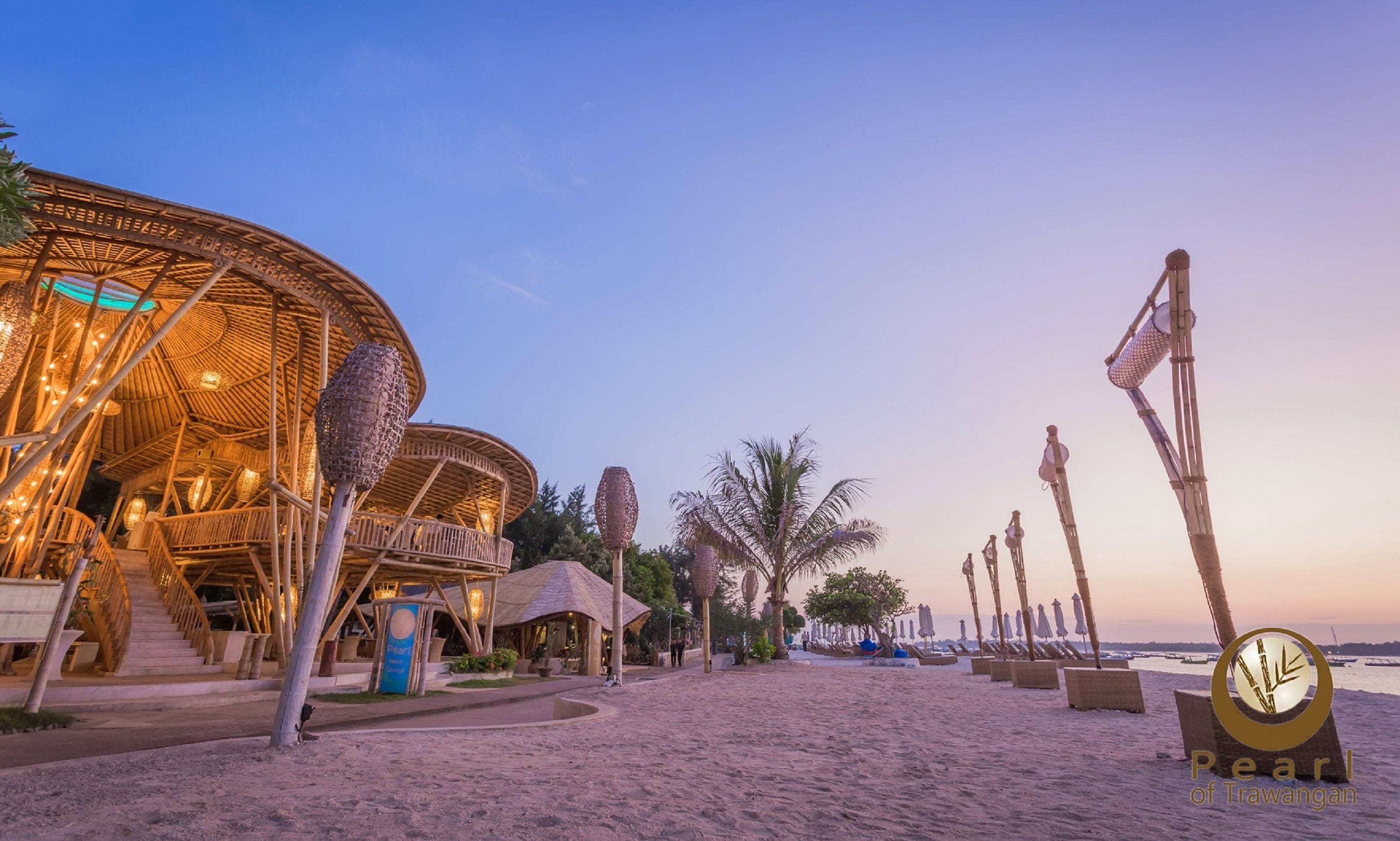 A beachside resort with a large, open-air structure featuring a thatched roof and string lights.