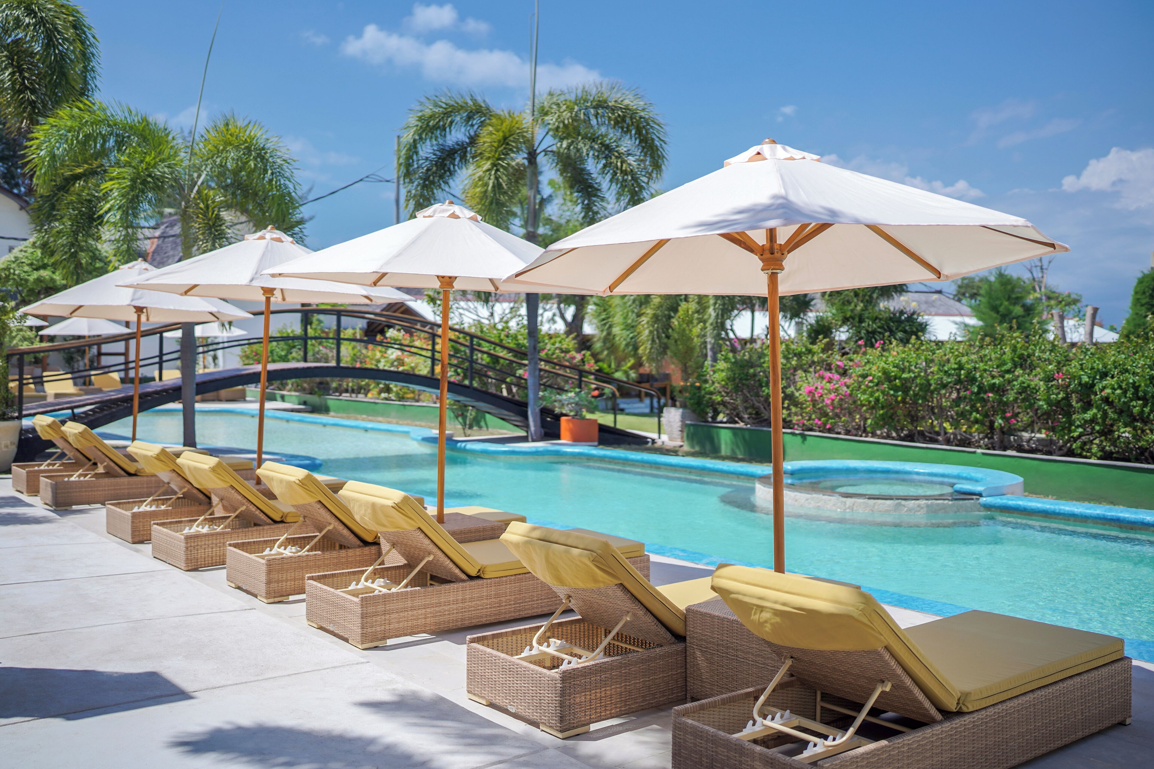 A poolside area with lounge chairs and umbrellas, a pool, and surrounding greenery.