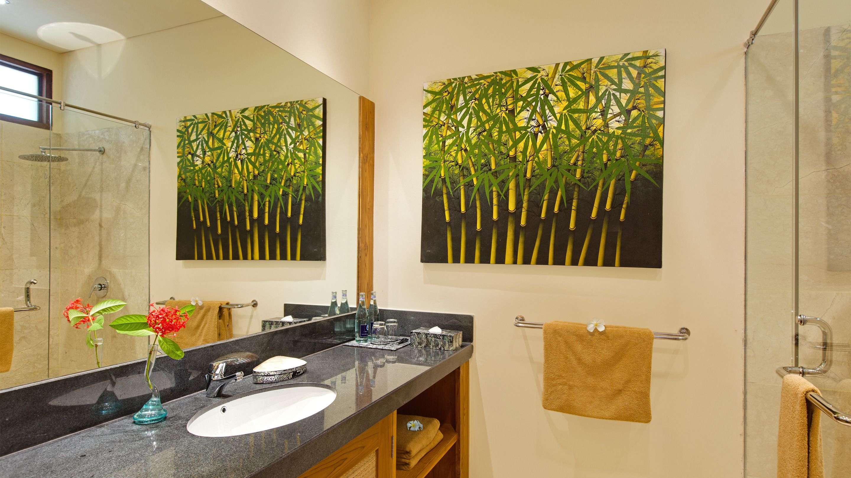 A bathroom with a large mirror, two wall-mounted paintings of bamboo, a sink, and a shower.