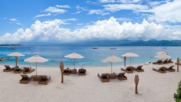 Na praia, areia branca, espreguiçadeiras, guarda-sóis