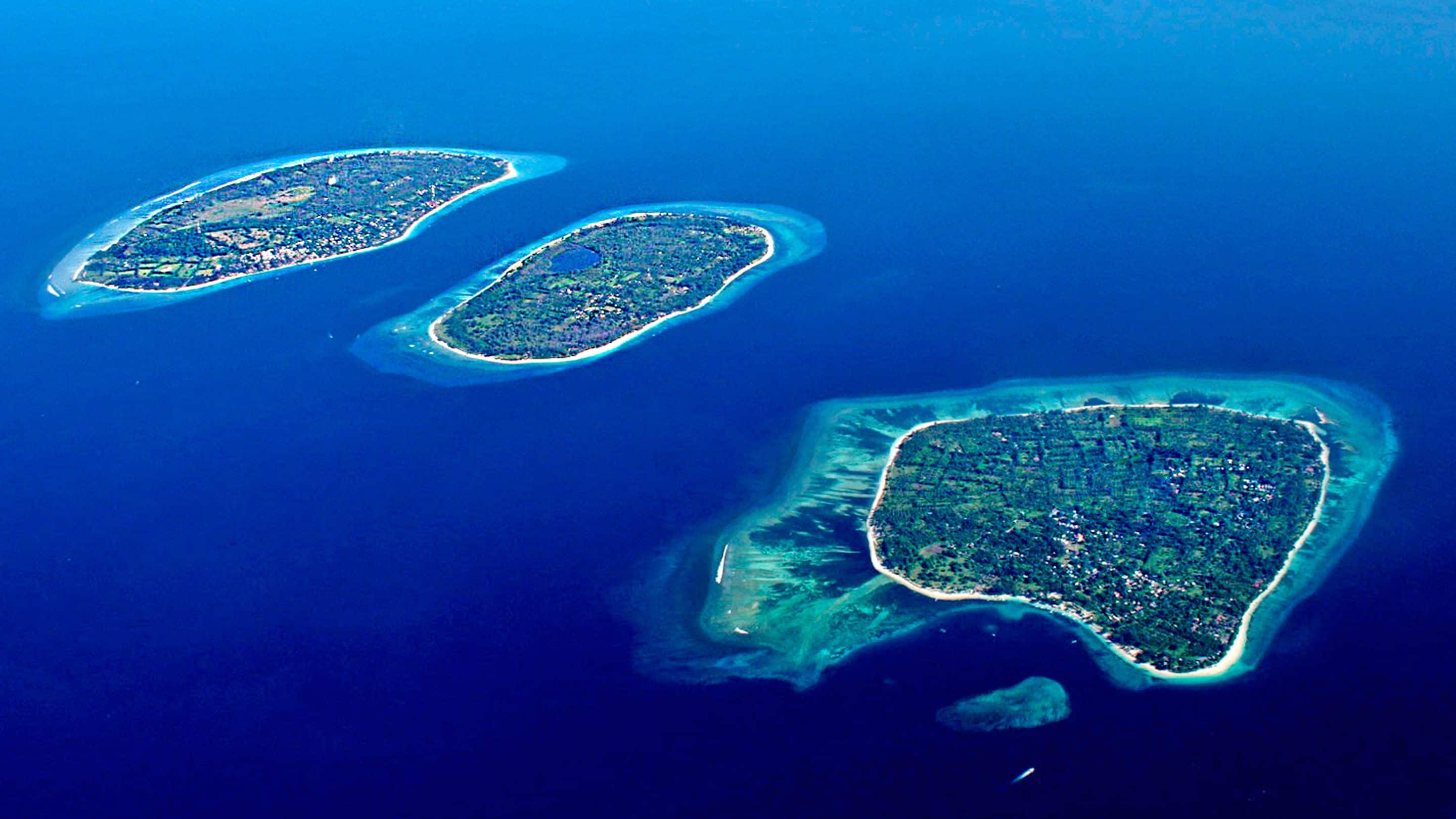Three small islands with clear blue waters and a dense vegetation cover.