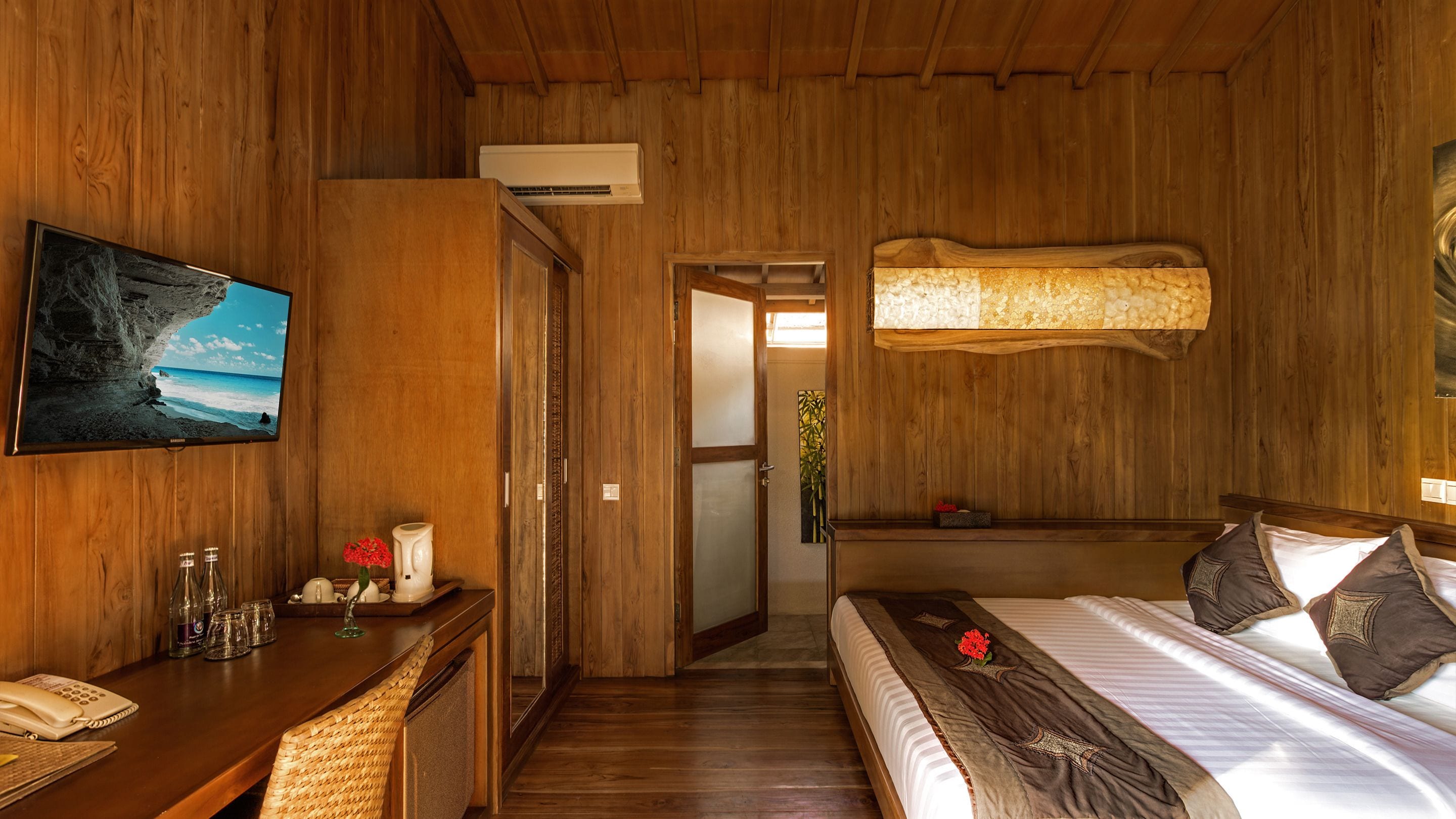 Une pièce en bois avec un lit, un bureau avec un téléphone, un tableau et un climatiseur fixé au mur.