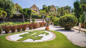 Un jardín bien cuidado con un diseño de seto circular, palmeras y diversos arbustos.