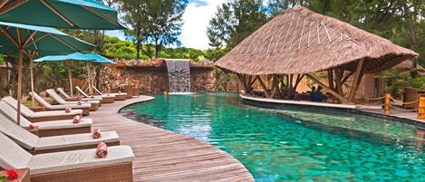 A pool area with lounge chairs, a thatched-roof structure, and a waterfall.