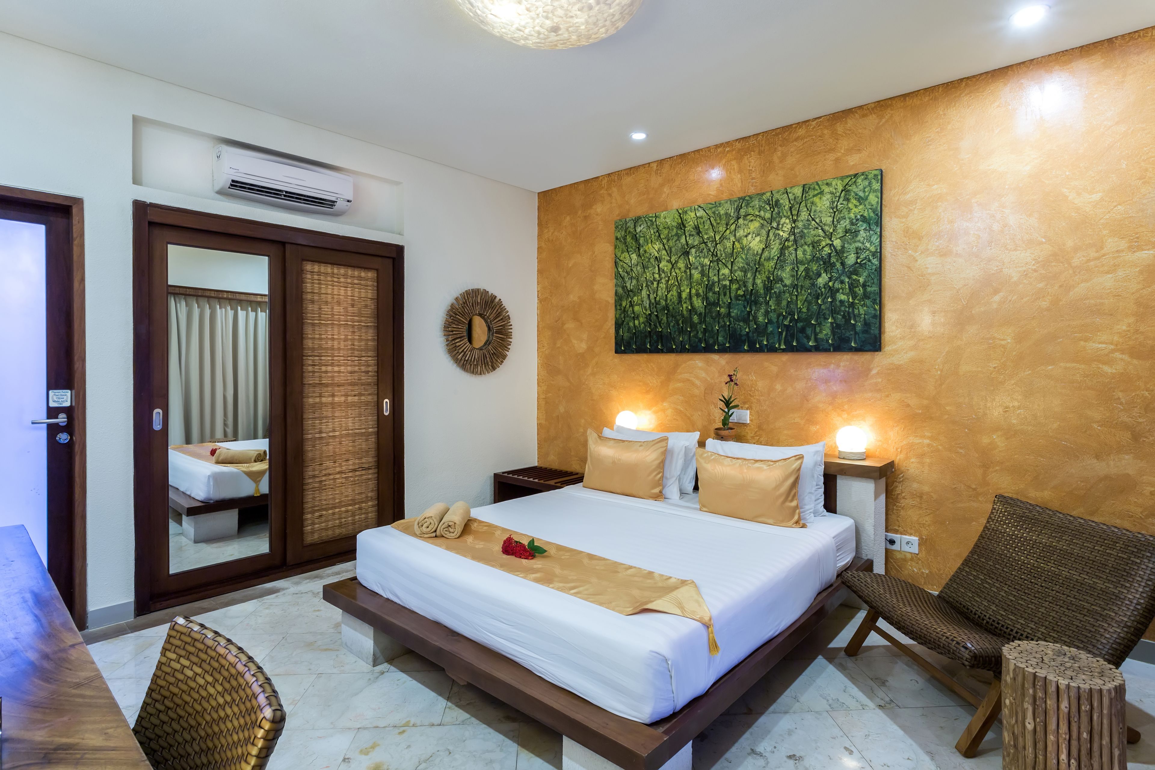 A hotel room with a large bed, a mirror, a wooden chair, and a wall-mounted painting.