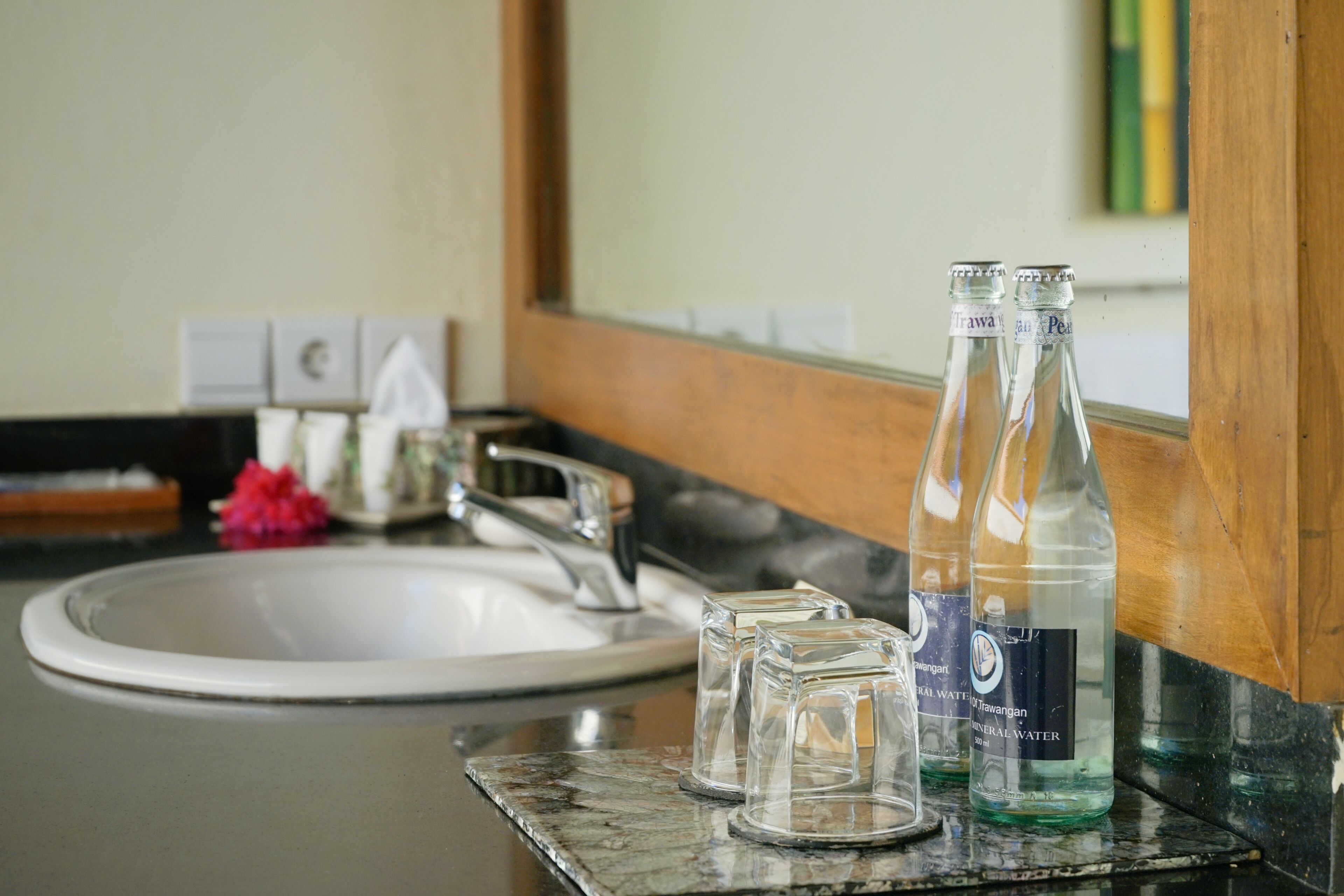 Un lavabo de baño con dos botellas de vidrio transparente etiquetadas como "Mineral Water" y un pequeño recipiente de vidrio.